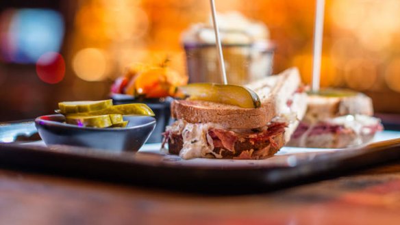 Reuben sandwich served with pickles and potato crisps.