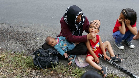 An Afghan migrant cleans a child's face as they rest on the side of a road after crossing the border from Serbia.