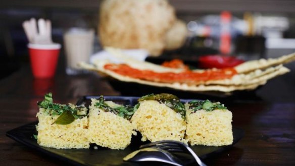 Khaman dhokla, in the foreground, is a steamed cake sprinkled with mustard seeds and curry leaves.