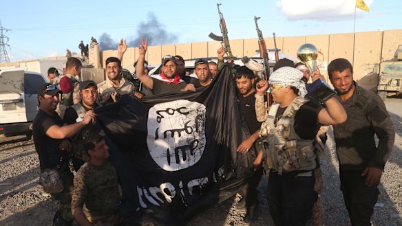Iraqi security forces and allied Shiite militiamen celebrate as they hold a flag of the Islamic State group they captured in Tikrit.