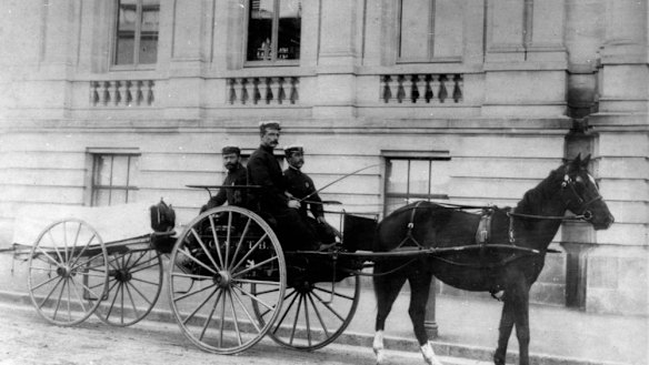 Ambulance officers posing on a buggy with a wheeled litter attached to it.