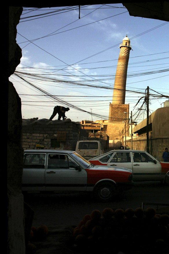 An electrician works on the roof of a shop in Mosul in 2003, in the background is the leaning minaret of the al-Nuri mosque.