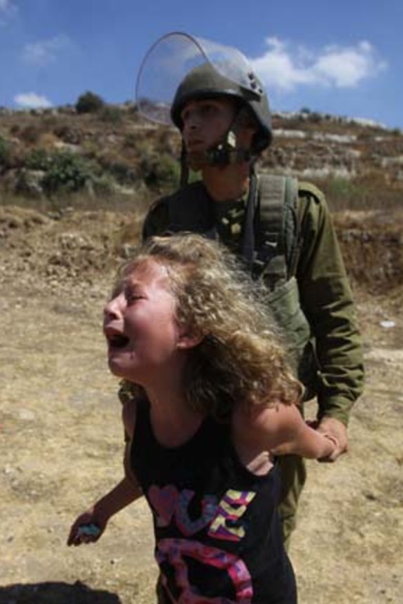 An Israeli soldier restrains a Palestinian girl crying over the arrest of her mother   during a  protest over land confiscation  in al-Nabi Saleh.