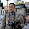 Japanese trucker Toshifumi Fujimoto holds his cameras in front of damaged buses in Aleppo's old city in Syria.